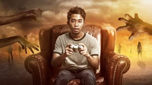 Man sitting on sofa with gaming remote in hand with zombie hands reaching towards him in the background.