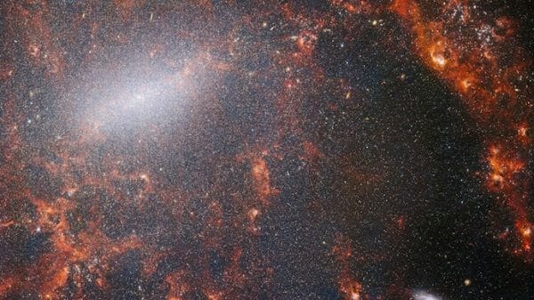 The image captured by the NIRCam instrument of the James Webb Space Telescope showcases the barred spiral galaxy NGC 5068, adorned with a vast assemblage of stars. The highest concentration of stars is found along the luminous central bar, accompanied by vibrant crimson gas clouds that are aglow, courtesy of youthful stars nestled within.
