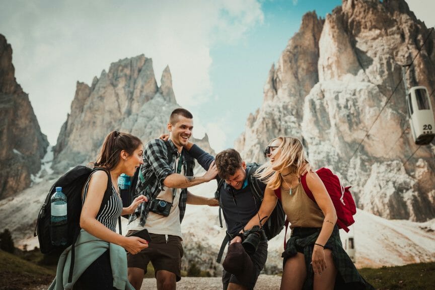 A group of friends in the mountains, all wearing travel clothing and backpacks. They are laughing together.