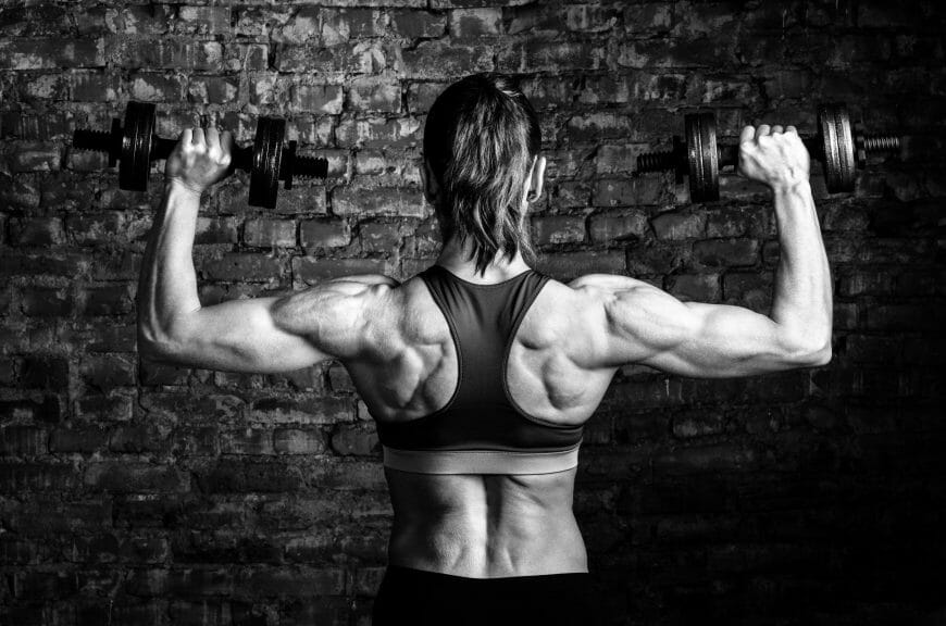 A women lifts hand-held weights with her muscular back toward the camera.