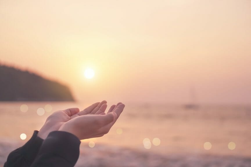 Woman places hands before a sunset.