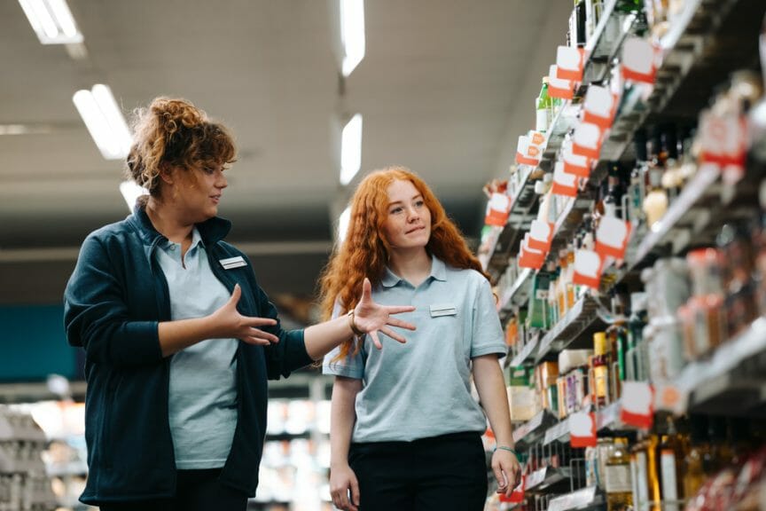 Grocery store manager training new female worker in the shop aisle.