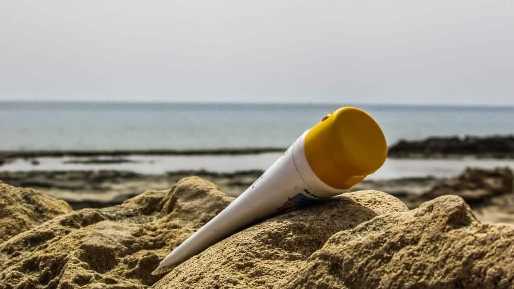 Bottle of sun cream laying on the sand on a beach.
