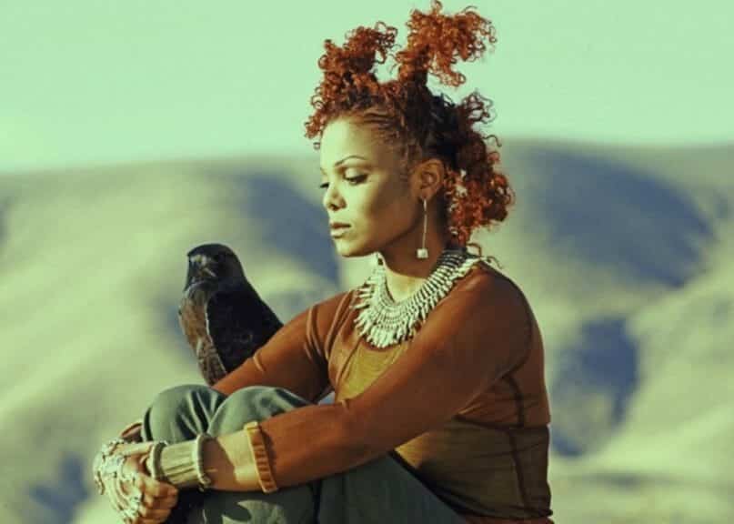 Janet Jackson sitting down next to a black bird.