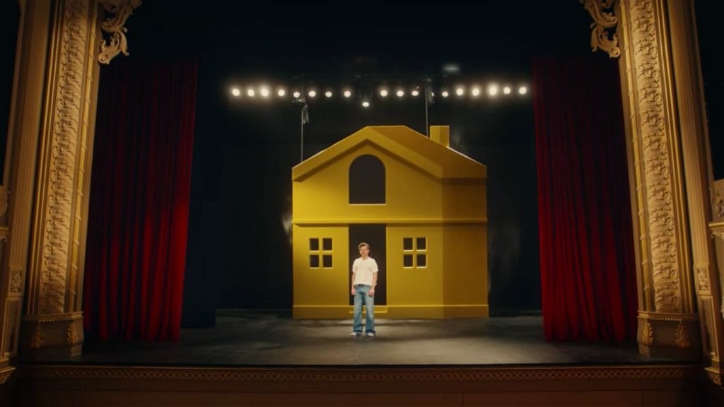 Harry Styles in his album 'Harry's House' teaser video, standing in front of a house cut-out.