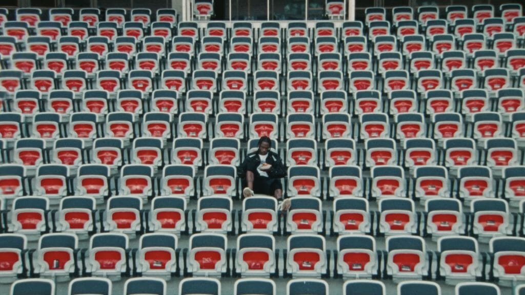 Travis Scott sitting in an empty stadium seating area.