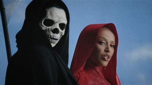 Doja cat wearing a red dress, standing next to the Grim Reaper. Both look at the camera.