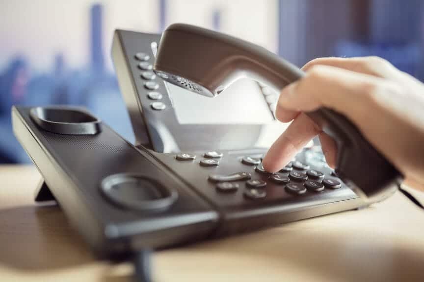 A hand types in a number on a landline.