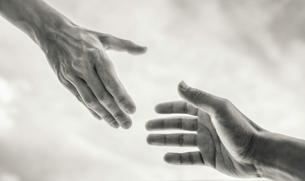 A black and white image of two hands trying to grab each other's from opposite ends. 