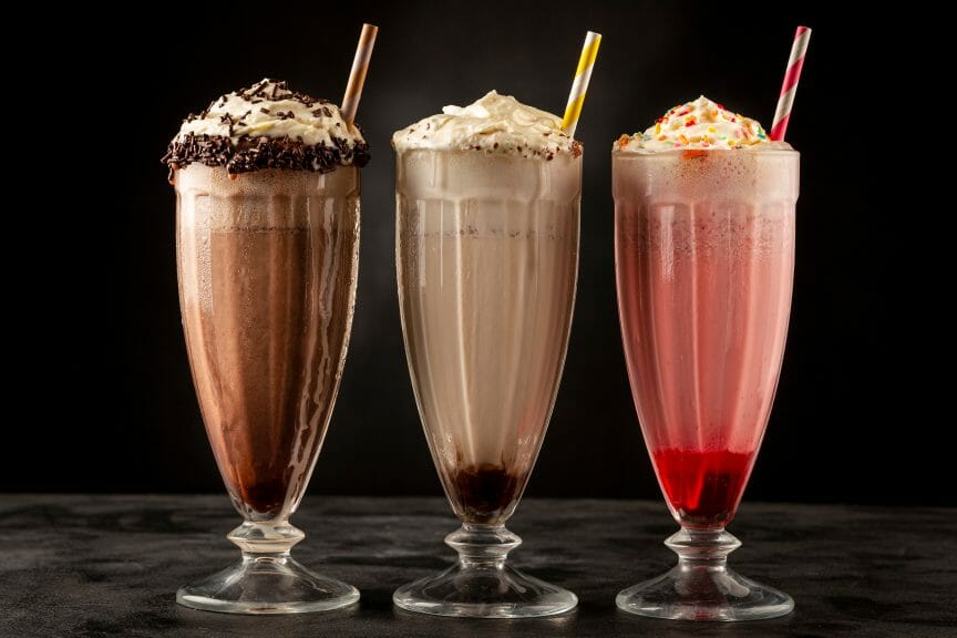 Chocolate, vanilla, and strawberry milkshake in a glass with a straw