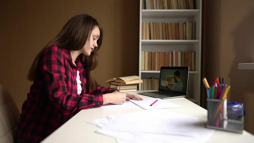 Student doing online school while taking notes on a physical worksheet.