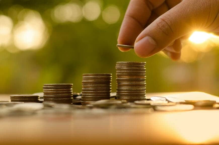 Four stacks of coins going from smallest to largest and a person's hand adding a coin to the largest stack.