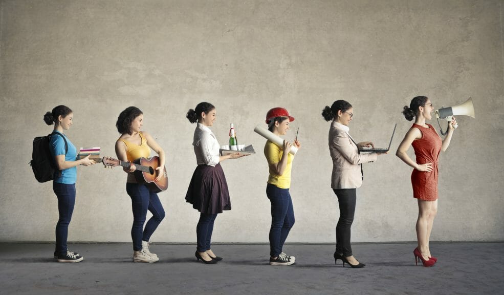 Six women who are the same person are in a single file line and each woman is dressed in a different career uniform. Starting from the left, the woman is dressed as a student, then the same women is dressed as a musician. The next is dressed as a waitress. The fourth woman is dressed as a construction worker, then the fifth woman is dressed as a businesswoman, and then the last woman is dressed as some sort of authority figure.