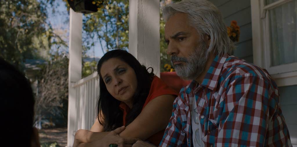 Image of Ari's parents, actress Veronica Falcon and actor Eugenio Derbez sitting together and looking at Ari. 