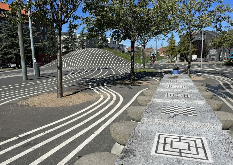 There are trees, a cycle path and a hill designed with stripes. Tables and chairs with popular board games painted on them.