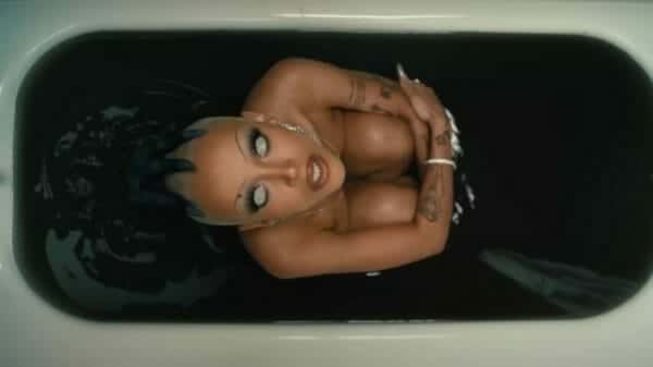 Doja Cat sitting in a bath tub filled with black liquid in her satanic 'Demons' music video.