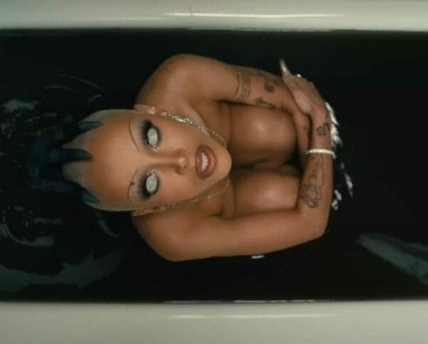 Doja Cat sitting in a bath tub filled with black liquid in her satanic 'Demons' music video.