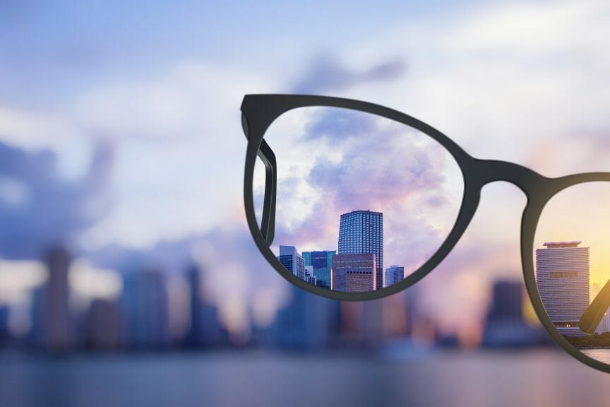 There's a blurry city in the background with a glasses frame that make the vision of the city clear. 