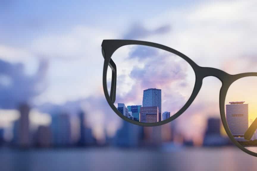 There's a blurry city in the background with a glasses frame that make the vision of the city clear.