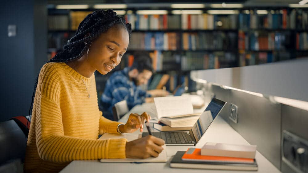 Female student working on a laptop and writing notes