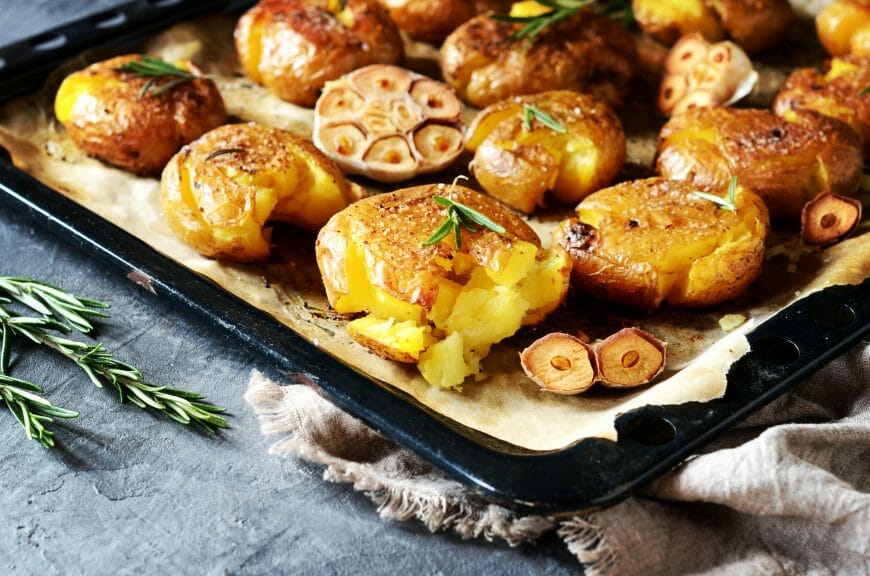 Smashed potatoes on a baking sheet with garlic and rosemary