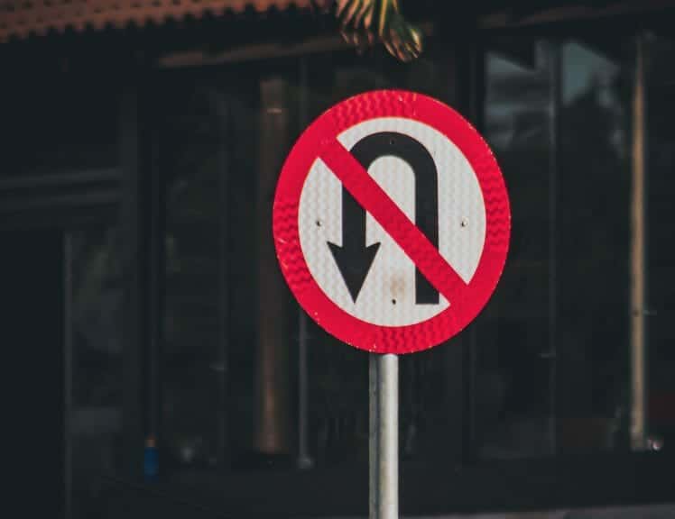 No returns road sign. Black and white arrow with red cross.