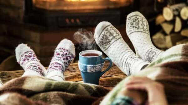 This is an image of two cozy socks and a warm mug of tea, with steam, trailing from it. The picture epitomises the coziness that hygge encapsulates