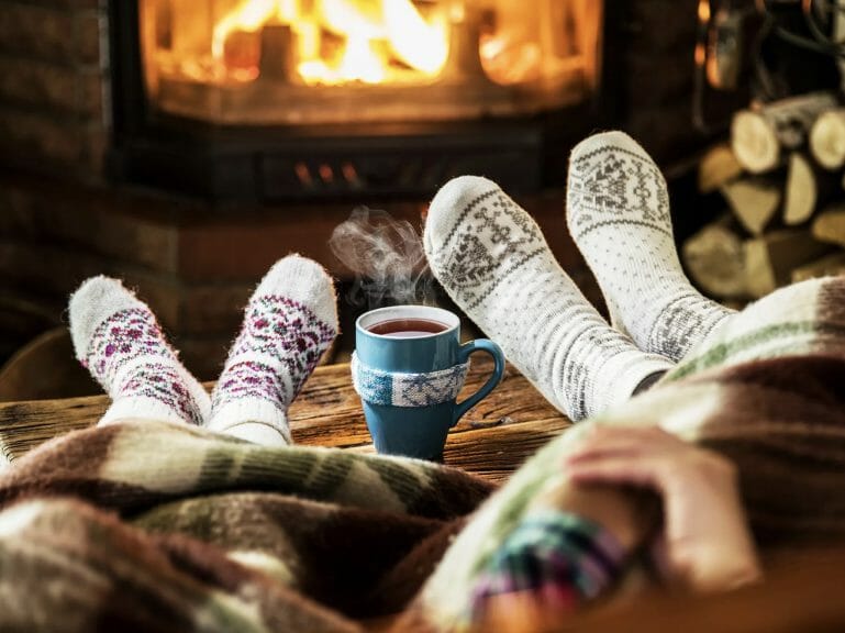This is an image of two cozy socks and a warm mug of tea, with steam, trailing from it. The picture epitomises the coziness that hygge encapsulates