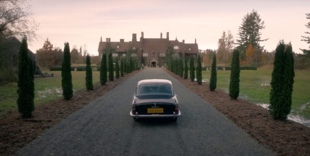 Image of a car approaching an imposing manor. 