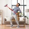 A man with headphones on dances with a broom in a tidy room.