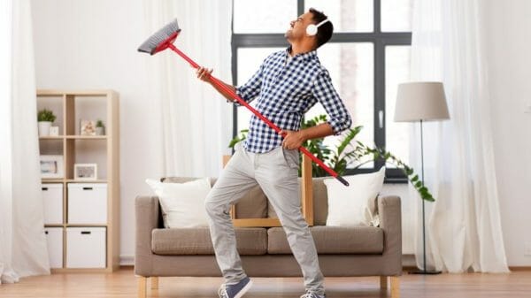 A man with headphones on dances with a broom in a tidy room.