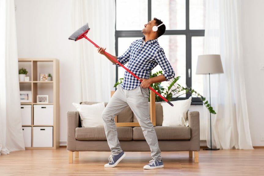 A man with headphones on dances with a broom in a tidy room.