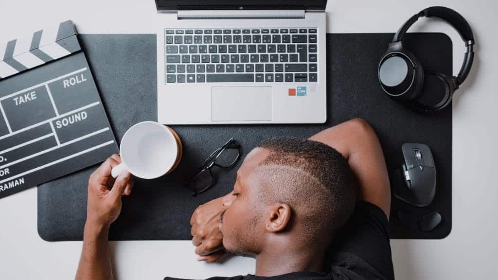 A man asleep on his desk with his coffee mug and computer.