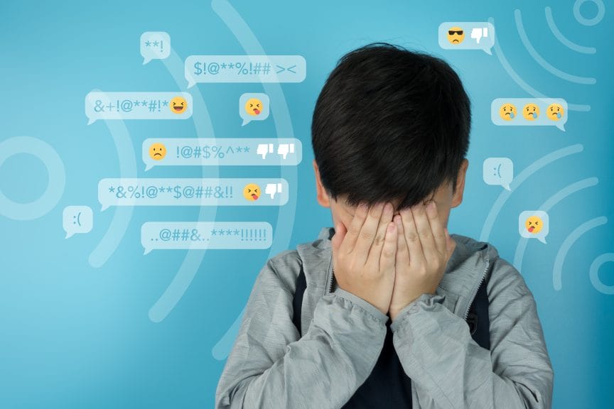 A boy with his face in his hands, over a background displaying various rude/mean social media messages and emojis.