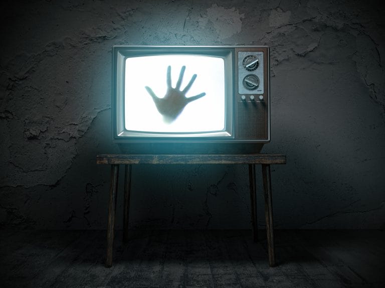 Hand on TV screen in a dark room.