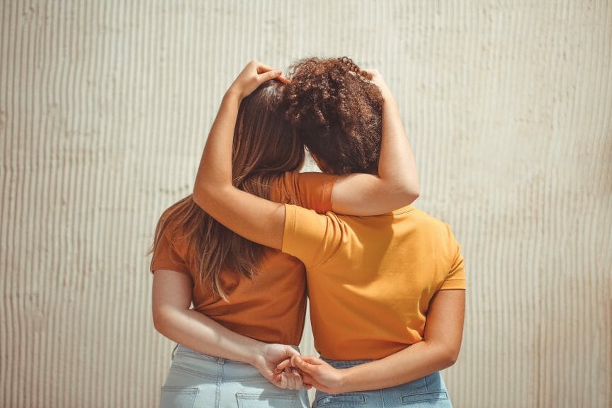 Two girl best friends embracing each other. The back of them are only seen. 