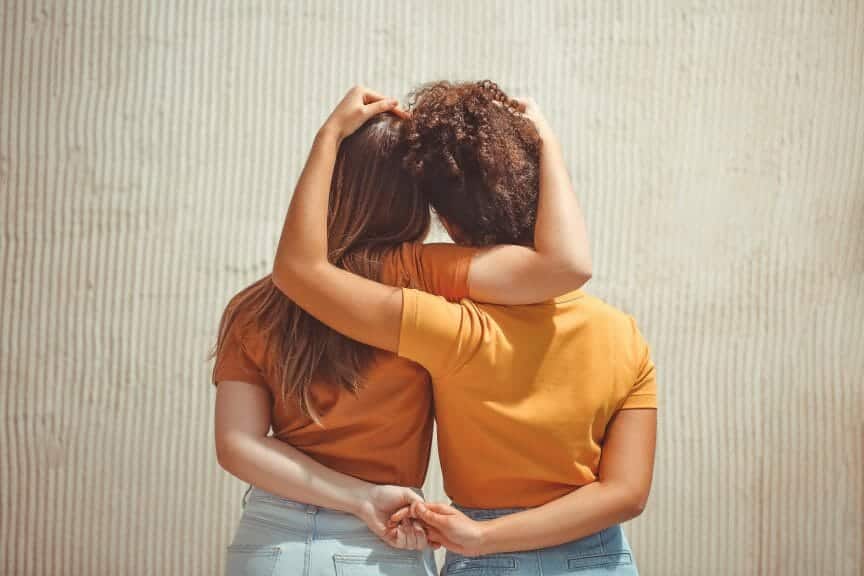 Two girl best friends embracing each other. The back of them are only seen. 