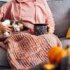 Image of a person sitting with a cat and mug on their lap.