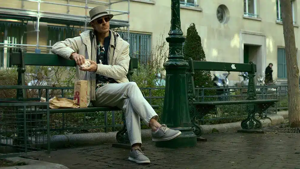 Michael Fassbender sitting on a park bench and eating McDonald's in a scene from 'The Killer.'