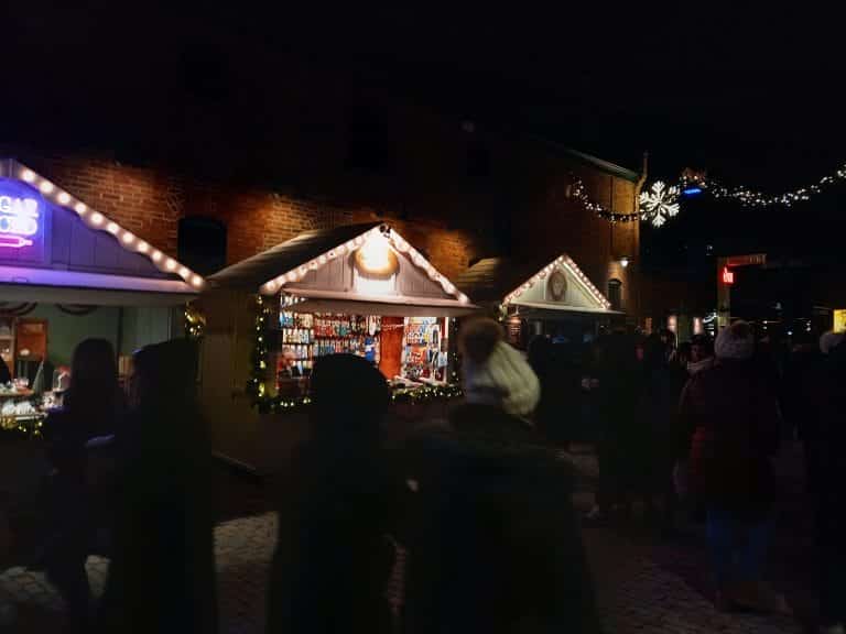 Little cabins with lights at night and people walking around them.