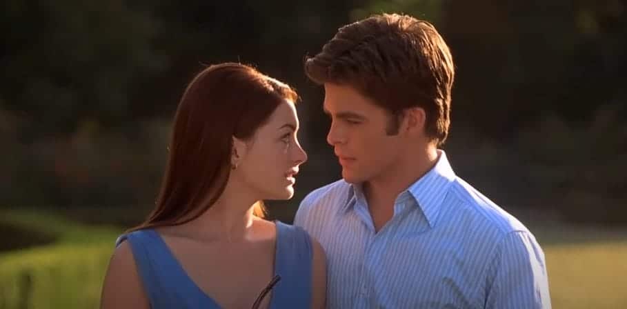 Mia Thermopolis, a girl with dark brown hair wearing a blue dress looks longingly at Nicholas Deveraux, a man wearing a blue and white striped shirt.