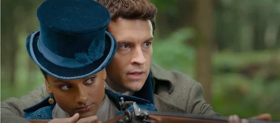 Antony Bridgerton, a man with brown hair wearing a suit looks into the distance as he helps Kate Sharma, a woman with dark hair and a green hat aim a gun.