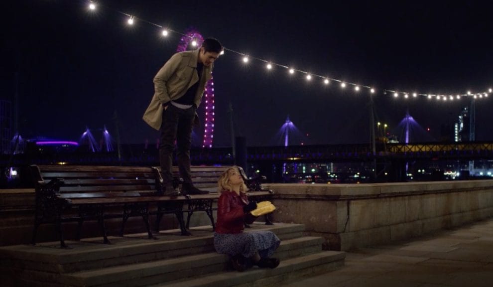 Main characters Kate and Tom at night with warm white lights hanging above them. 