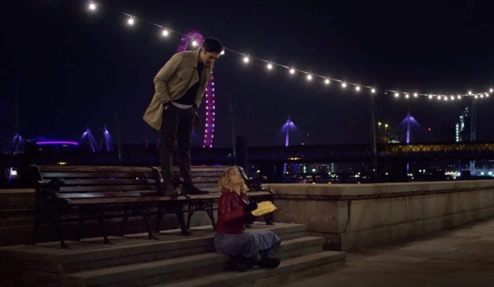 Main characters Kate and Tom at night with warm white lights hanging above them. 