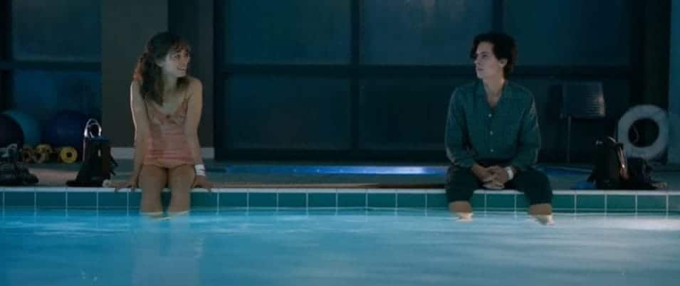 Stella, a woman wearing a pink dress, sits on the edge of a pool beside Will, a boy wearing a grey-blue shirt.