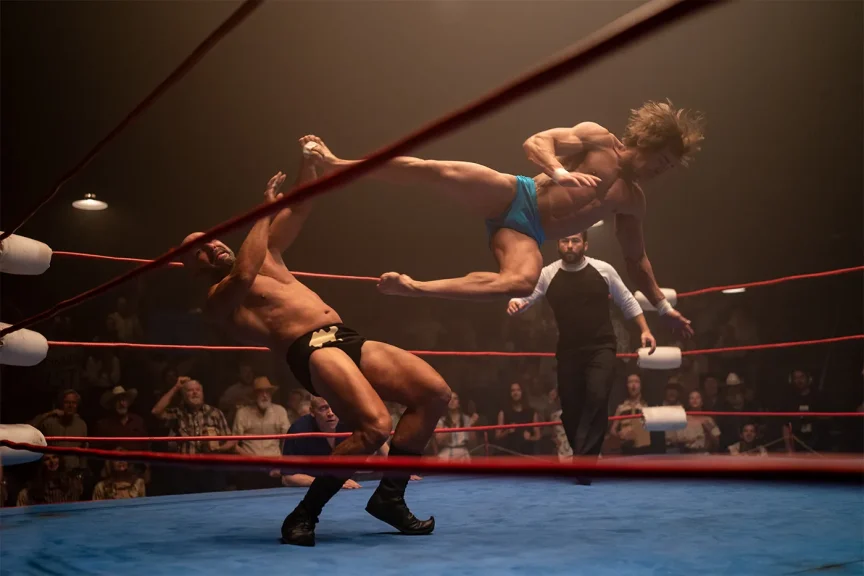 Preview image from 'The Iron Claw' in which Zac Efron is midair after having kicked an opponent in a wresting arena. 