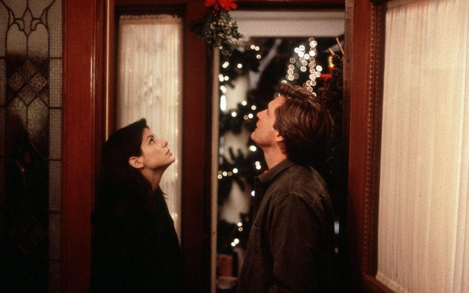 Sandra Bullock and Bill Pullman stand under mistletoe in the film While You Were Sleeping