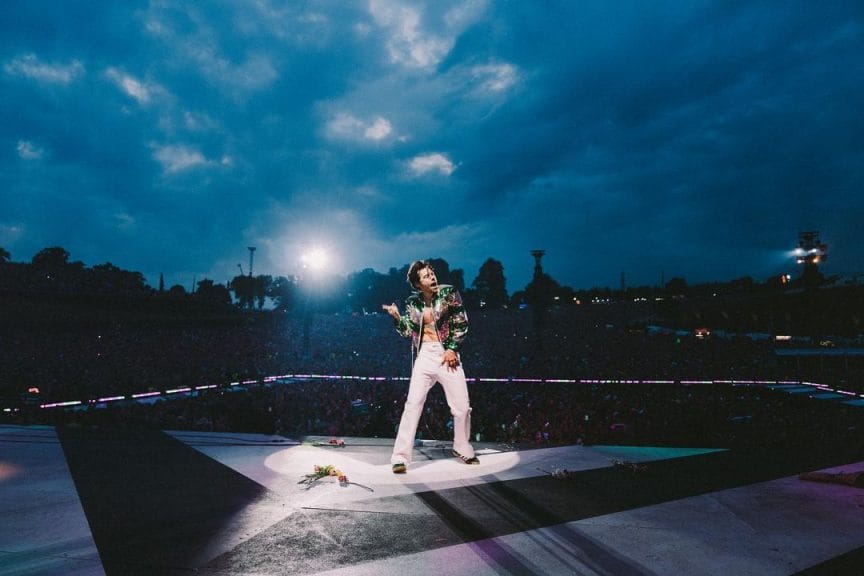 Harry styles dancing on stage during a tour performance that pushes stereotypes of gender. 