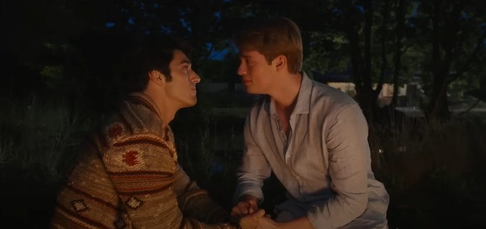 Alex, a boy with dark hair, and Henry, a boy with blonde hair, sit facing each other in the woods.