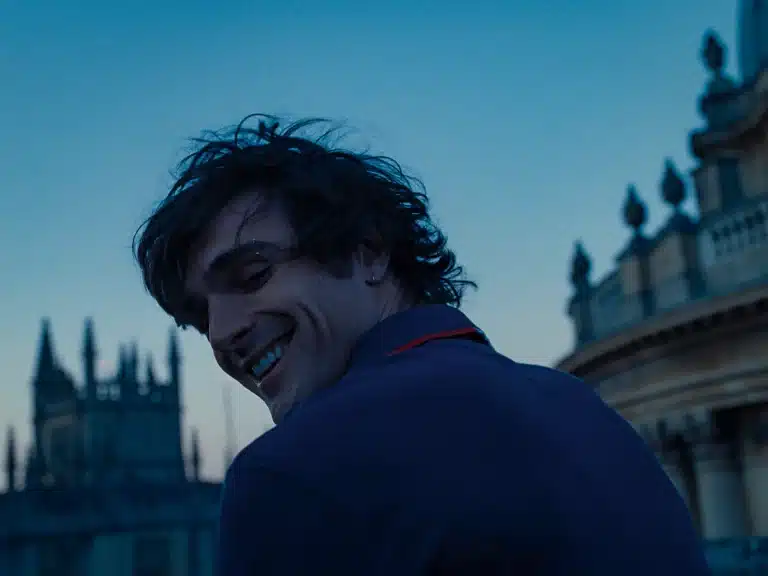 Still from 'Saltburn' of Jacob Elordi facing forward and looking back toward the camera, smiling. 